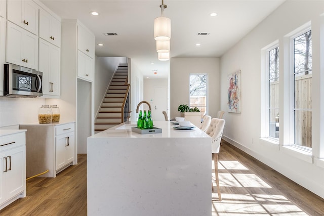 kitchen with pendant lighting, white cabinetry, backsplash, an island with sink, and light wood-type flooring