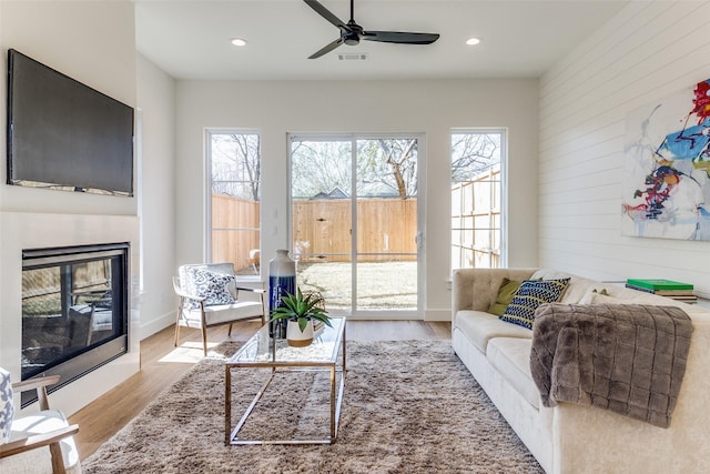 living room with light hardwood / wood-style flooring, ceiling fan, and wood walls