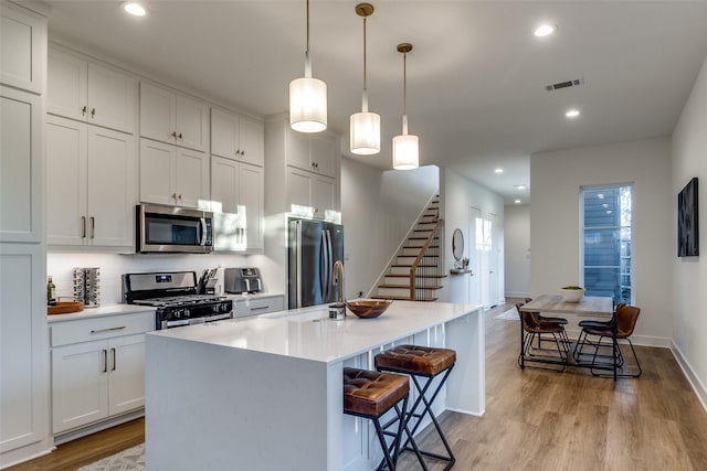 kitchen featuring pendant lighting, white cabinets, a kitchen island with sink, stainless steel appliances, and light wood-type flooring