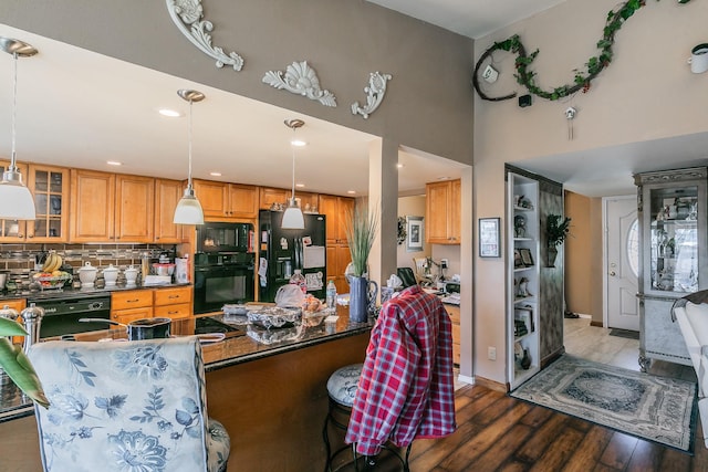 kitchen with pendant lighting, hardwood / wood-style floors, backsplash, a towering ceiling, and black appliances