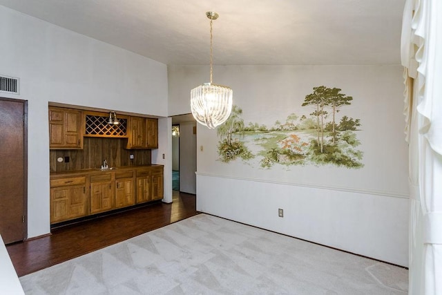 unfurnished dining area with wood-type flooring, vaulted ceiling, a chandelier, and indoor bar