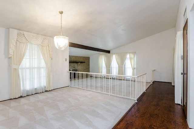 unfurnished room with beamed ceiling, a brick fireplace, hardwood / wood-style floors, and an inviting chandelier