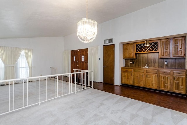 interior space with lofted ceiling, indoor wet bar, a notable chandelier, and dark carpet