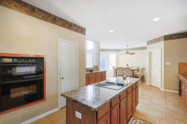 kitchen featuring a kitchen island, dark stone countertops, light tile patterned floors, ceiling fan, and black appliances