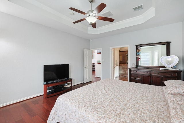 bedroom with ensuite bath, dark wood-type flooring, ceiling fan, a tray ceiling, and ornamental molding