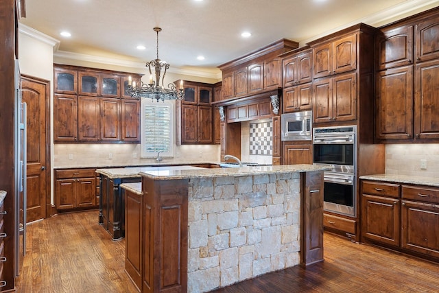 kitchen featuring dark wood-type flooring, stainless steel appliances, an island with sink, and hanging light fixtures