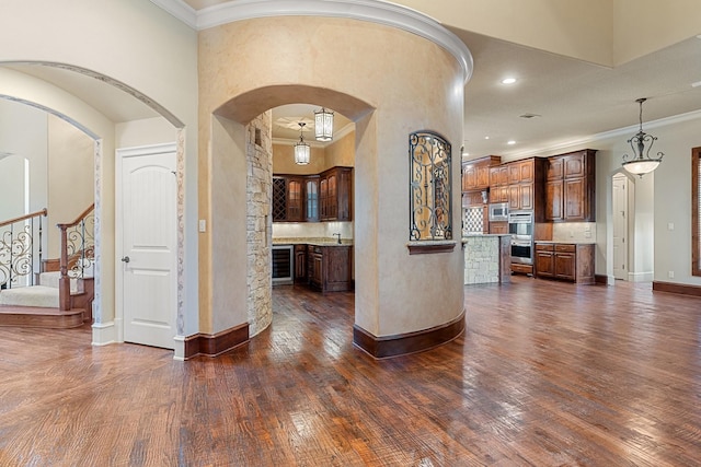 interior space with a center island, ornamental molding, appliances with stainless steel finishes, dark hardwood / wood-style floors, and pendant lighting