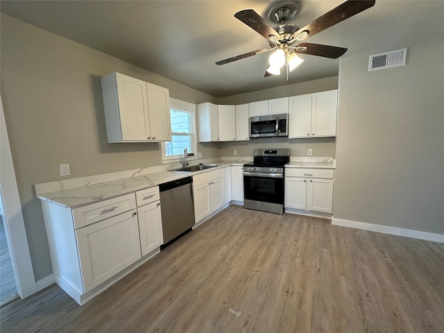 kitchen with sink, light hardwood / wood-style flooring, appliances with stainless steel finishes, light stone countertops, and white cabinets