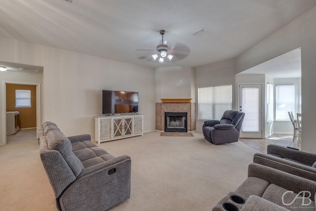 living room with a tiled fireplace, light colored carpet, and ceiling fan