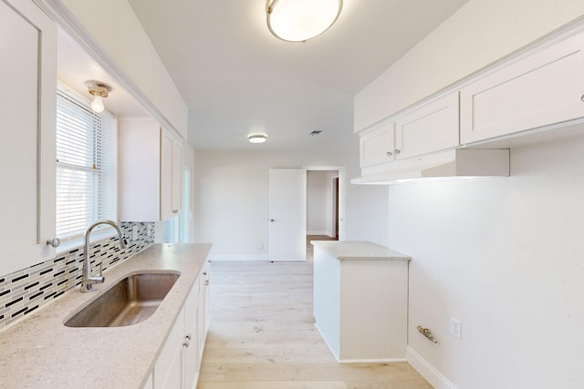 kitchen featuring tasteful backsplash, white cabinetry, sink, light stone countertops, and light wood-type flooring