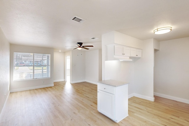 kitchen featuring ceiling fan, white cabinetry, light stone countertops, light hardwood / wood-style floors, and a textured ceiling