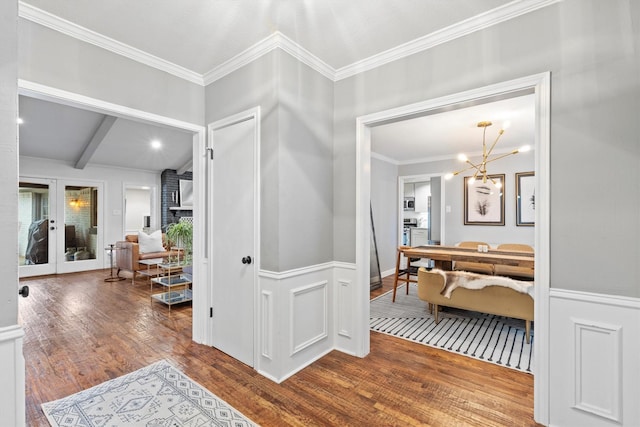 hall with beamed ceiling, wood finished floors, an inviting chandelier, wainscoting, and crown molding