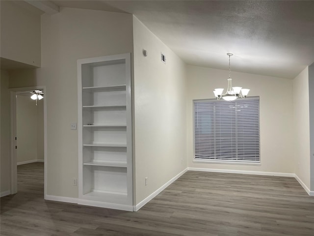 unfurnished dining area with ceiling fan with notable chandelier, built in features, lofted ceiling, hardwood / wood-style flooring, and a textured ceiling