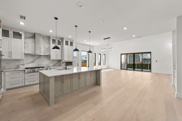 kitchen featuring sink, hanging light fixtures, stainless steel gas cooktop, a center island with sink, and wall chimney range hood