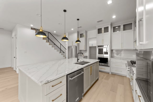 kitchen featuring pendant lighting, sink, stainless steel appliances, white cabinets, and a center island with sink