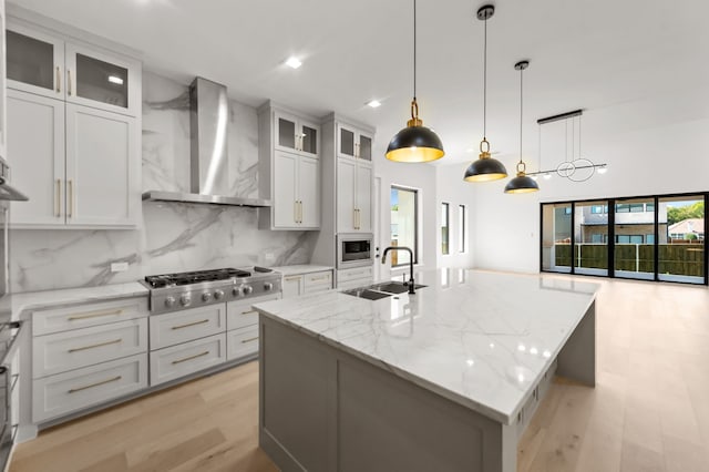 kitchen featuring sink, appliances with stainless steel finishes, white cabinetry, an island with sink, and wall chimney exhaust hood