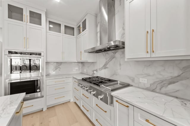 kitchen with light stone counters, white cabinets, stainless steel appliances, and wall chimney range hood