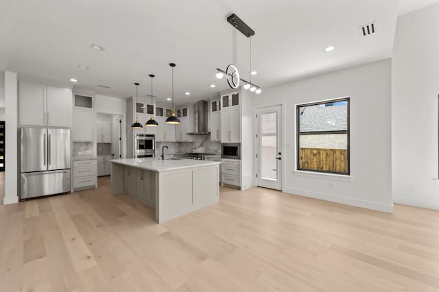 kitchen featuring white cabinetry, hanging light fixtures, appliances with stainless steel finishes, a large island, and wall chimney range hood