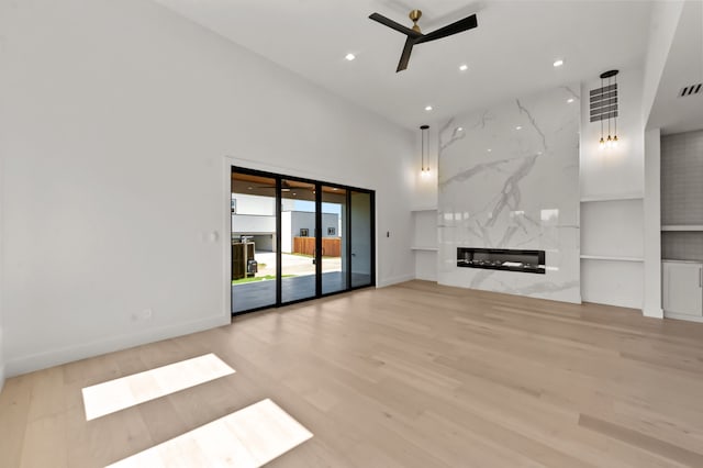 unfurnished living room with a towering ceiling, ceiling fan, light hardwood / wood-style floors, a premium fireplace, and built in shelves