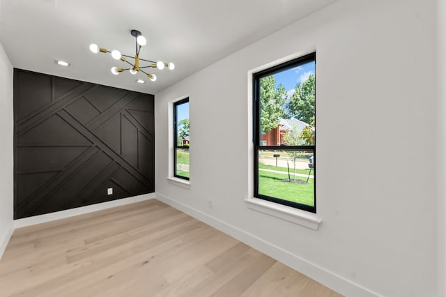 spare room with a chandelier and light wood-type flooring