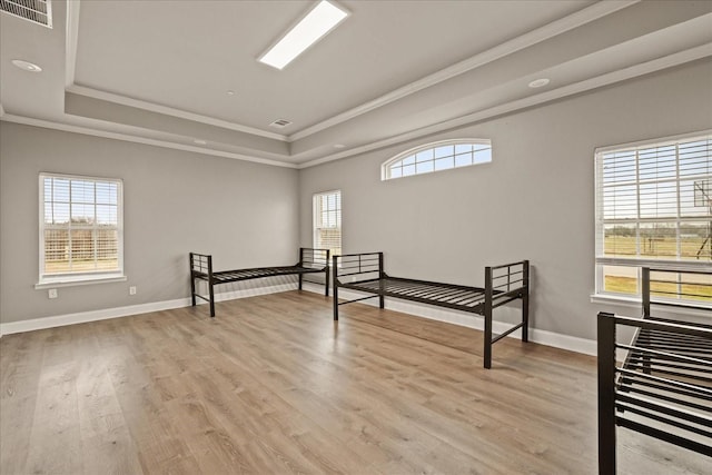 bedroom with multiple windows, a tray ceiling, and light wood-type flooring