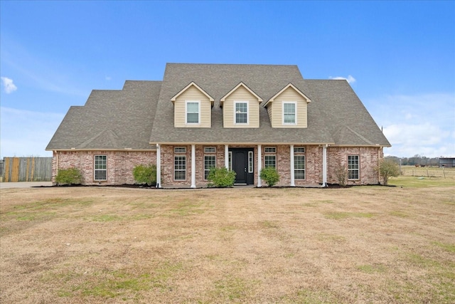 cape cod-style house featuring brick siding, fence, a front lawn, and roof with shingles