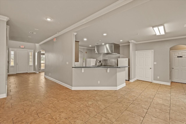 kitchen featuring wall chimney range hood, ornamental molding, a kitchen bar, kitchen peninsula, and white fridge