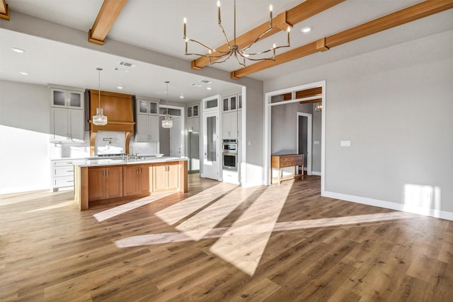 kitchen featuring stainless steel appliances, a large island with sink, white cabinets, decorative light fixtures, and beamed ceiling