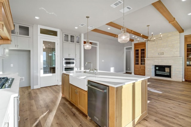 kitchen with beamed ceiling, an island with sink, sink, white cabinets, and stainless steel appliances