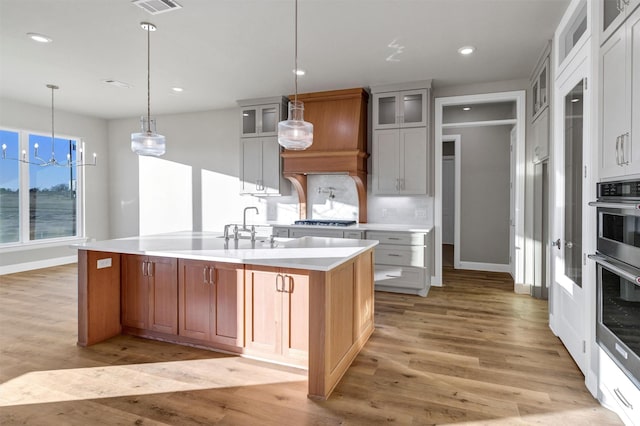 kitchen with white cabinets, decorative backsplash, a large island with sink, and light wood-type flooring