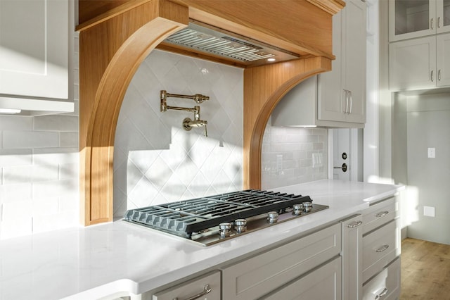 kitchen with backsplash, light hardwood / wood-style floors, stainless steel gas cooktop, and white cabinets