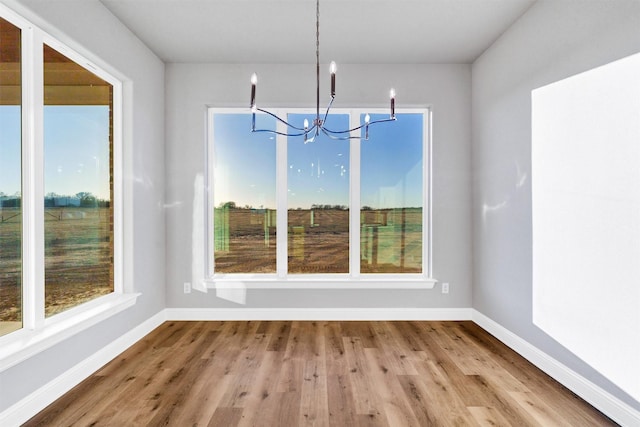 unfurnished dining area with a notable chandelier, wood-type flooring, and a healthy amount of sunlight