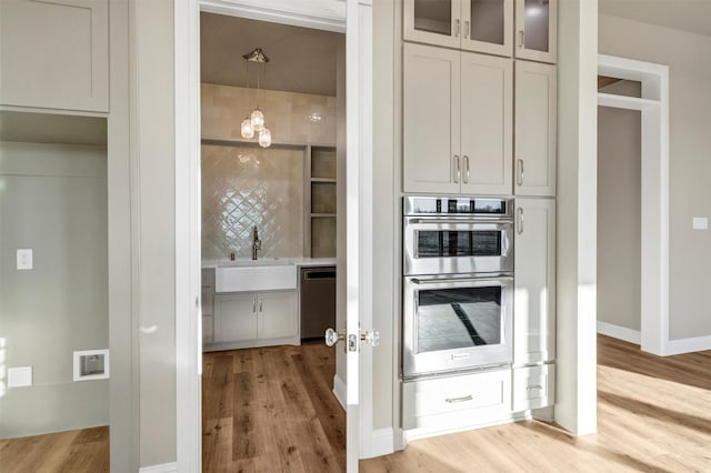 kitchen with appliances with stainless steel finishes, sink, hanging light fixtures, and light wood-type flooring