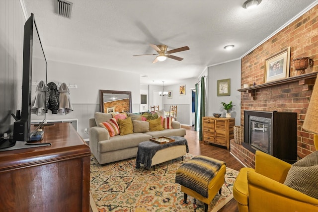 living room with ceiling fan with notable chandelier, a fireplace, hardwood / wood-style flooring, crown molding, and a textured ceiling