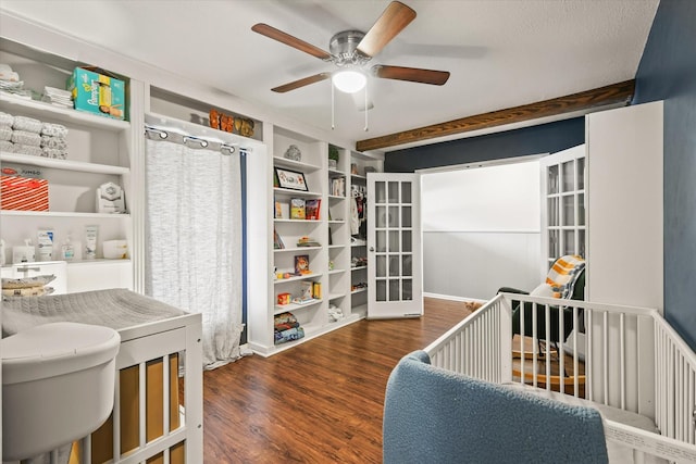 bedroom featuring a nursery area, dark wood-type flooring, and ceiling fan