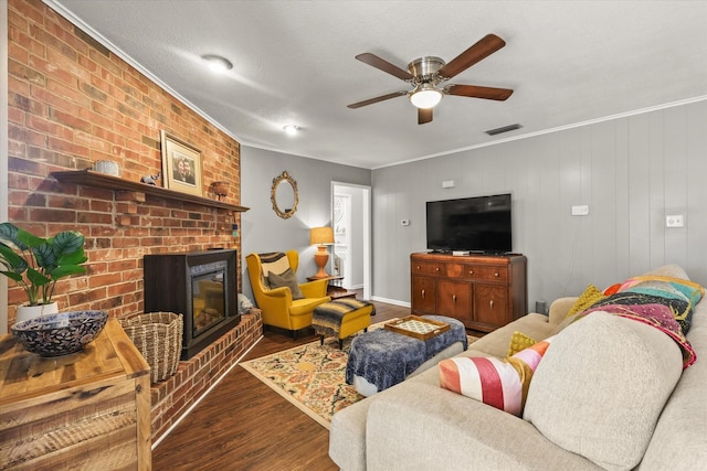 living room with ceiling fan, crown molding, a brick fireplace, dark wood-type flooring, and a textured ceiling