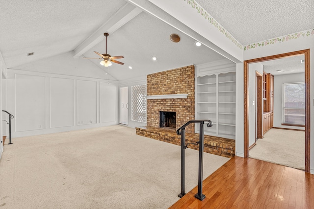 carpeted living room featuring a brick fireplace, built in shelves, lofted ceiling with beams, and a textured ceiling