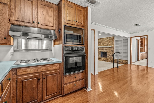 kitchen with stainless steel microwave, black oven, a fireplace, stovetop, and a textured ceiling