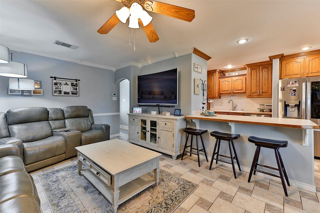 living room featuring ceiling fan, ornamental molding, and sink