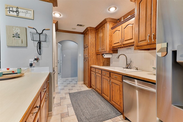 kitchen featuring sink, tasteful backsplash, a textured ceiling, ornamental molding, and appliances with stainless steel finishes