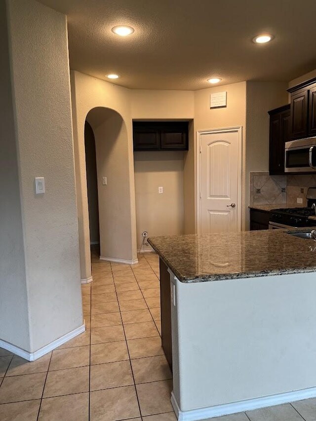14125 Rabbit Brush Ln, Fort Worth, TX 76052 - kitchen featuring appliances with stainless steel finishes, arched walkways, dark stone counters, recessed lighting, and light tile patterned flooring