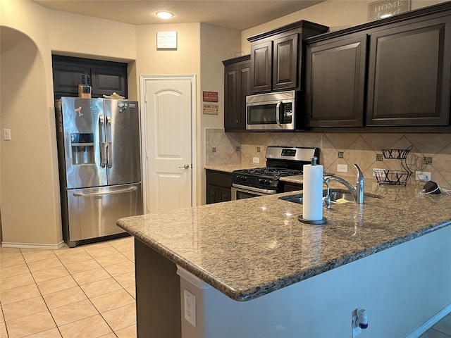 kitchen featuring sink, dark stone countertops, stainless steel appliances, tasteful backsplash, and kitchen peninsula