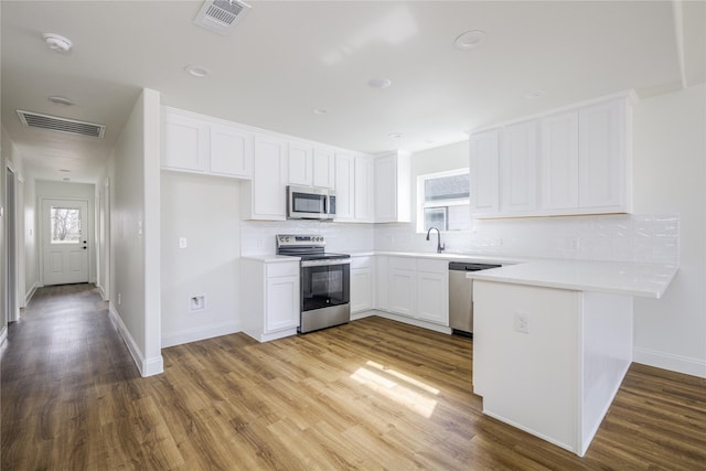 kitchen featuring wood-type flooring, sink, white cabinets, decorative backsplash, and stainless steel appliances