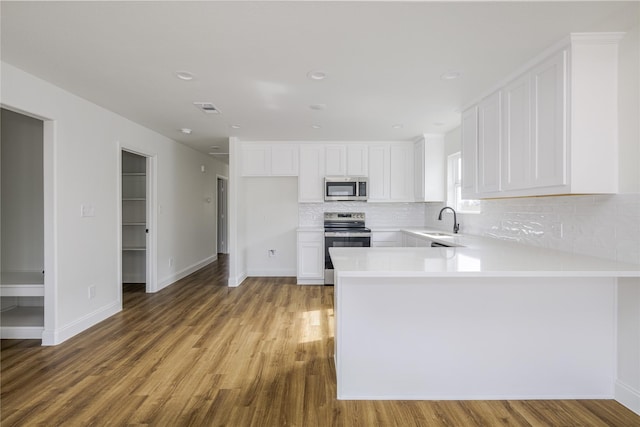 kitchen with sink, tasteful backsplash, stainless steel appliances, hardwood / wood-style floors, and white cabinets