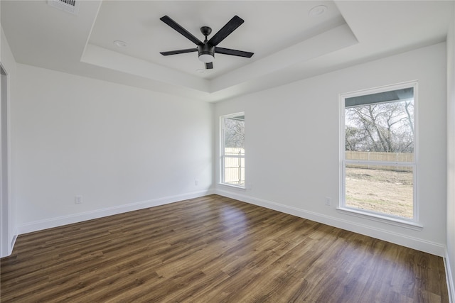 empty room with ceiling fan, dark hardwood / wood-style floors, and a raised ceiling