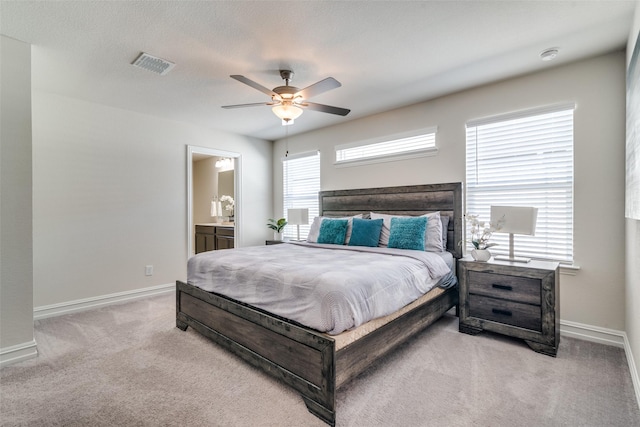 bedroom with light carpet, ensuite bath, and ceiling fan