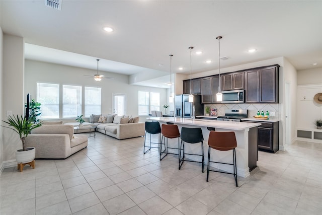 kitchen with dark brown cabinetry, a breakfast bar area, a center island with sink, appliances with stainless steel finishes, and backsplash