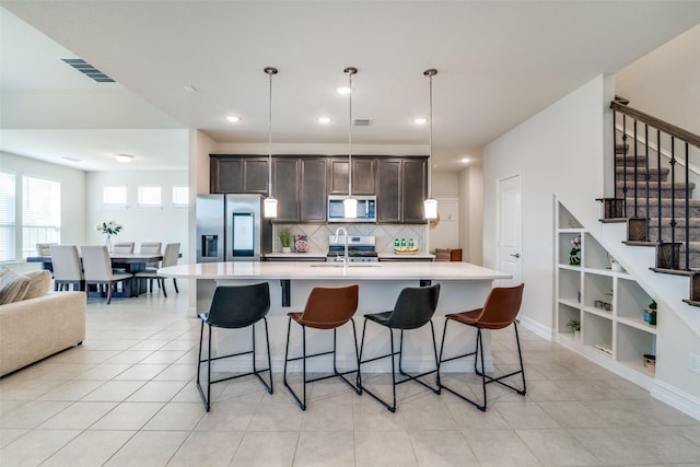 kitchen with appliances with stainless steel finishes, pendant lighting, sink, a kitchen island with sink, and dark brown cabinetry