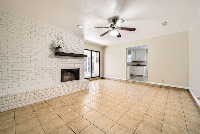 unfurnished living room featuring light tile patterned flooring, a textured ceiling, ceiling fan, brick wall, and a fireplace