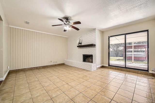 unfurnished living room featuring ceiling fan, a brick fireplace, light tile patterned floors, and a textured ceiling